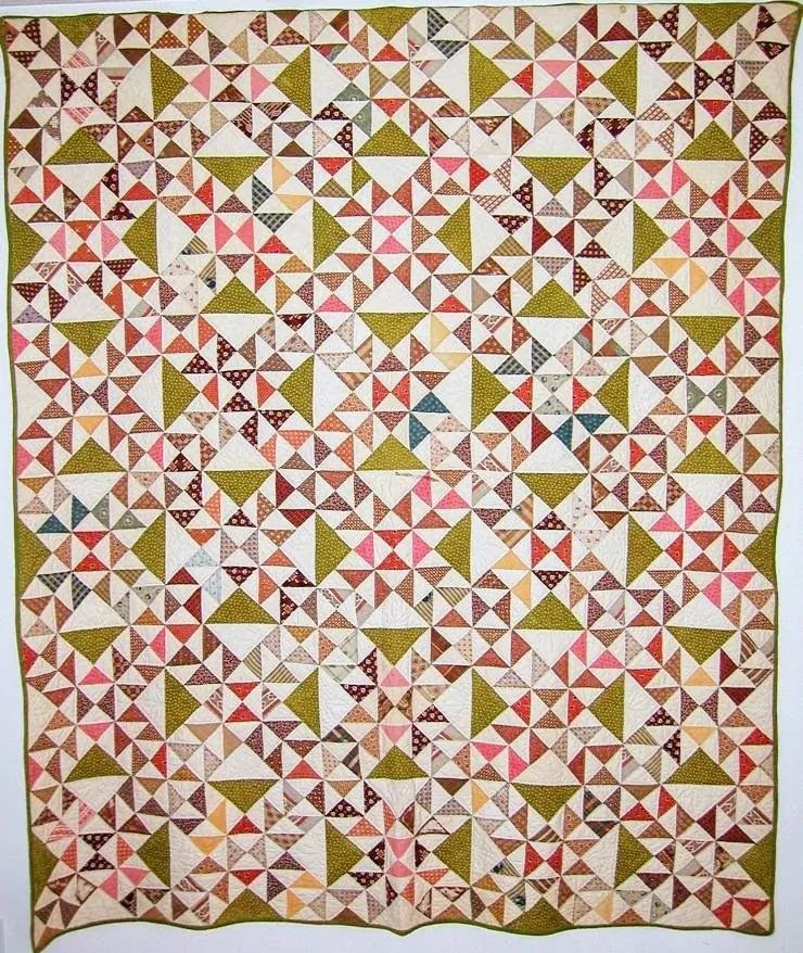 A handmade quilt with a repeating geometric pinwheel pattern in shades of pink, green, tan, cream, and touches of blue—this colorful, intricate design beautifully celebrates quilt history and our quilting heritage.