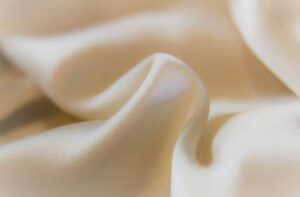 satin-weave Close-up of smooth, cream-colored silk fabric with soft folds and a gentle sheen, highlighting its glossy, luxurious texture.