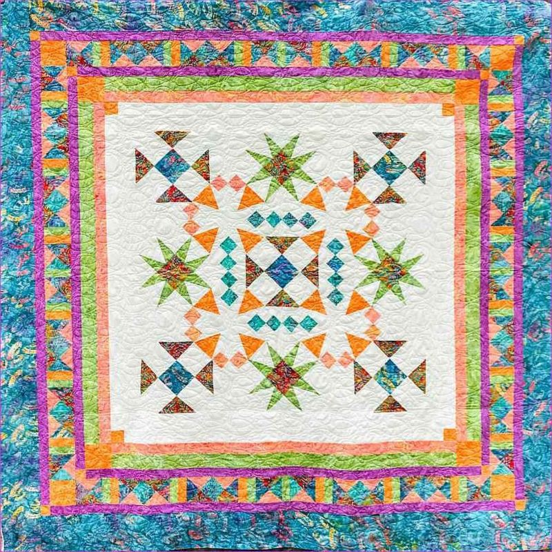 A colorful patchwork quilt with intricate geometric patterns in blue, orange, green, and pink. The quilt has multiple borders and a central design featuring star and diamond shapes on a white background.