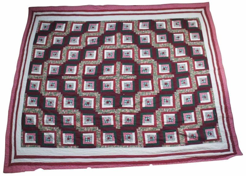 A handmade quilt featuring a repeating pattern of red, green, black, and white squares bordered with red and white stripes. The design creates a geometric, almost three-dimensional effect.