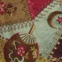 A patchwork quilt section with embroidered floral patterns, a lantern, intricate decorative stitching, and a crescent moon with a star, featuring earthy red, green, and blue fabric pieces.