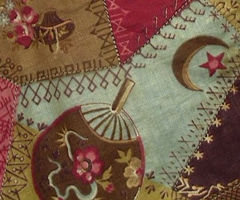A patchwork quilt section with embroidered floral patterns, a lantern, intricate decorative stitching, and a crescent moon with a star, featuring earthy red, green, and blue fabric pieces.