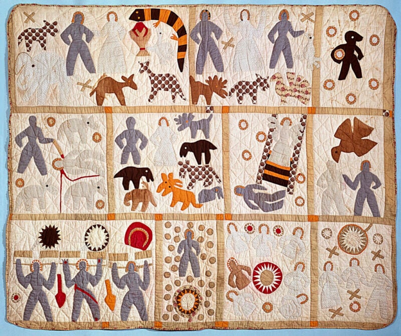 Harriet-Powers-Bible-Quilt A colorful patchwork quilt featuring appliqué human and animal figures, geometric shapes, and circles, arranged in panels across a light background with visible stitching.