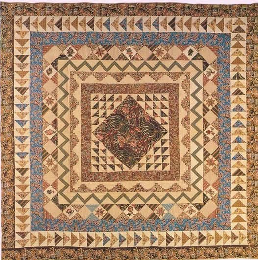 A patchwork quilt with intricate geometric border patterns in earthy tones and floral prints, featuring triangles, zigzags, and a central diamond motif surrounded by multiple patterned frames.