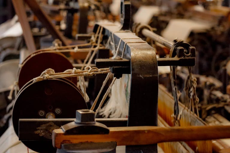 Photo by Oliver Morgan Media A detailed close-up of an antique loom showcasing the threading process in a textile production setting.
