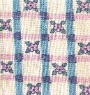 Close-up of a woven fabric with a checkered pattern in blue and pink lines, featuring small floral motifs at the intersects on an off-white background.