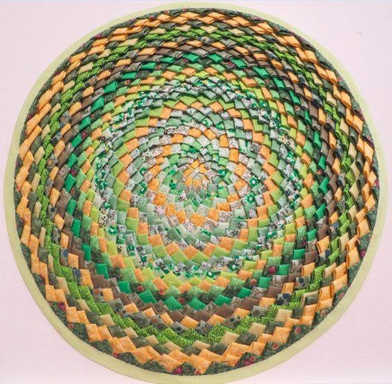 A circular mosaic pattern made of small, square tiles in shades of green, yellow, and orange, arranged in a spiral formation, creating a three-dimensional optical illusion.