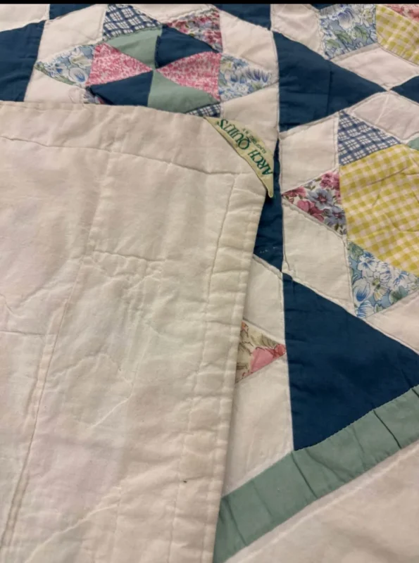 A handmade quilt with a colorful geometric patchwork pattern and blue, yellow, pink, and floral fabrics, partially folded to show the plain white underside.