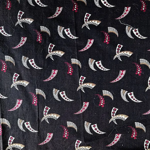 Black fabric with a repeating pattern of stylized, fan-shaped motifs in white, gold, and red, scattered evenly across the surface. Some motifs have dotted accents. The texture of the fabric is visible.