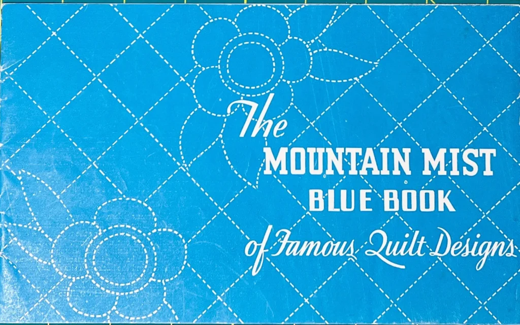 Blue quilted cover with white stitched flower designs. Text reads: The Mountain Mist Blue Book of Famous Quilt Designs.