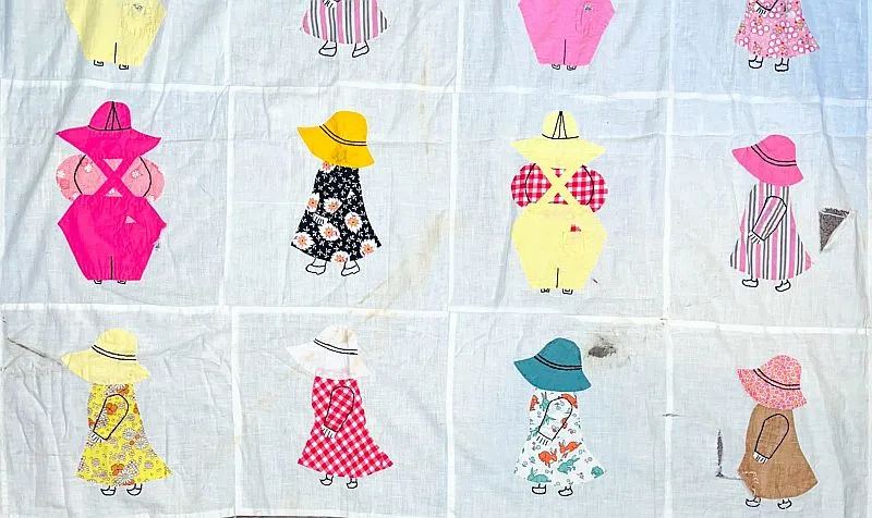 Sunbonnet-Sue-Overall-Sam-800 A quilt with twelve squares, each featuring a girl in a dress and hat made from different patterned fabrics. The figures are outlined simply, with no faces, on a white background. Some spots and stains are visible, offering glimpses into the quilt history about its age and use—please contact us for further details.