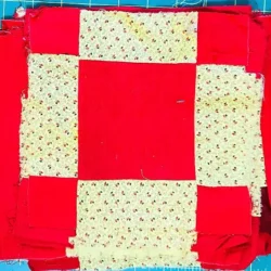 A stack of quilt blocks made of red and cream patterned fabric arranged in a square-in-a-square design, placed on a teal cutting mat with gridlines.