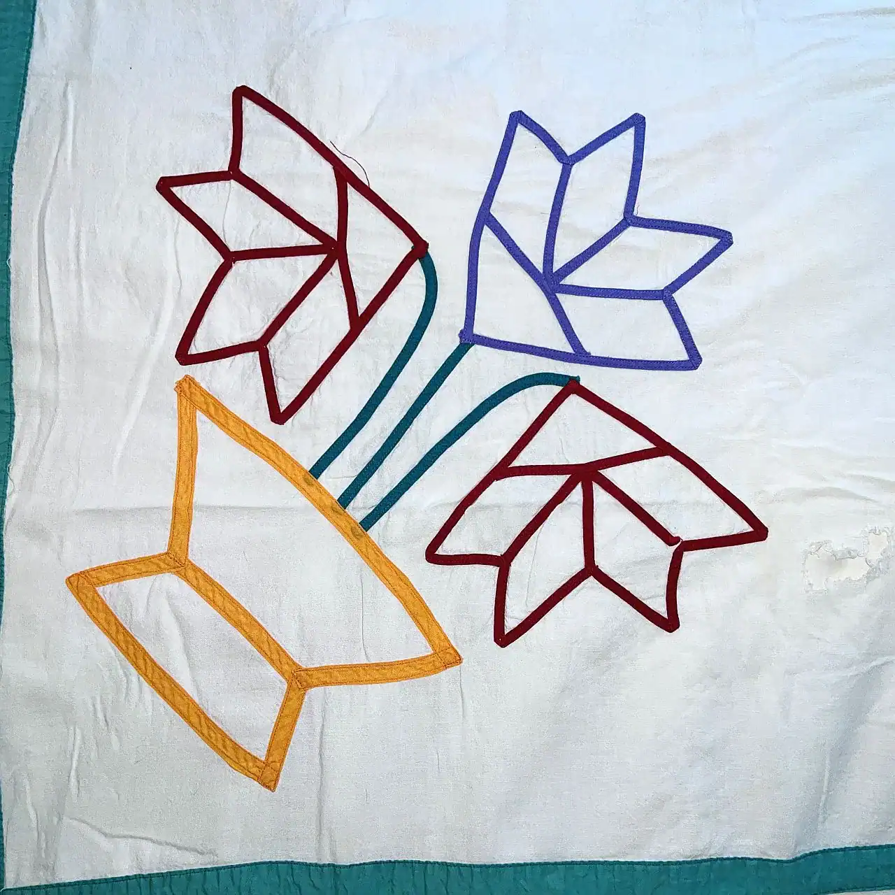 bias-tape-basket A quilt square with a yellow vase and three stylized flowers—two red and one blue—on a white background, outlined with colored fabric strips.