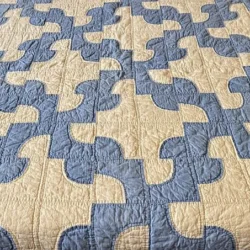 A quilt featuring an interlocking blue and cream geometric pattern, with curved and angular shapes creating a repeating, puzzle-like design across the surface.