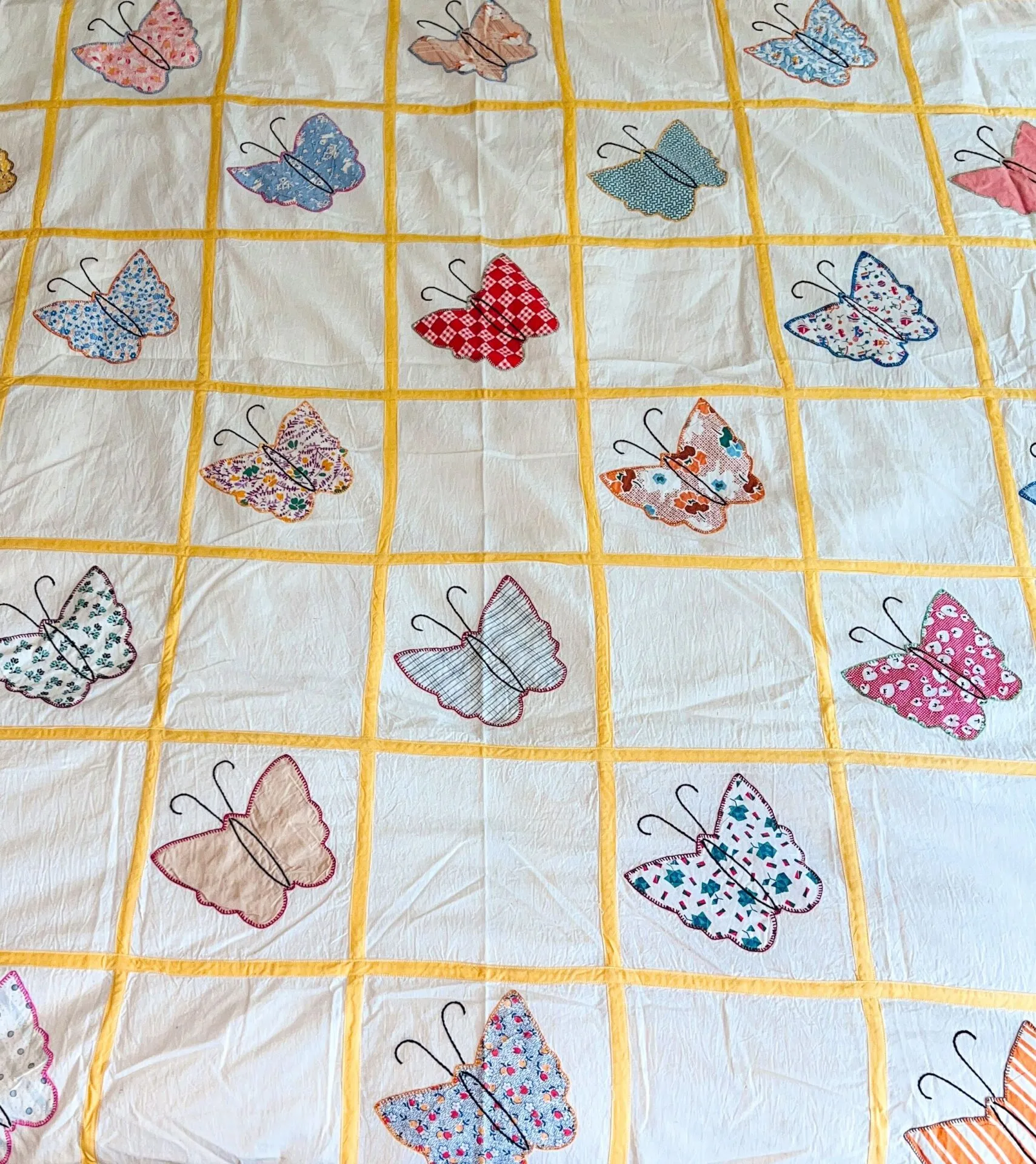 A quilt with a grid of yellow-bordered squares, each square featuring a colorful butterfly made from different patterned fabrics on a white background.