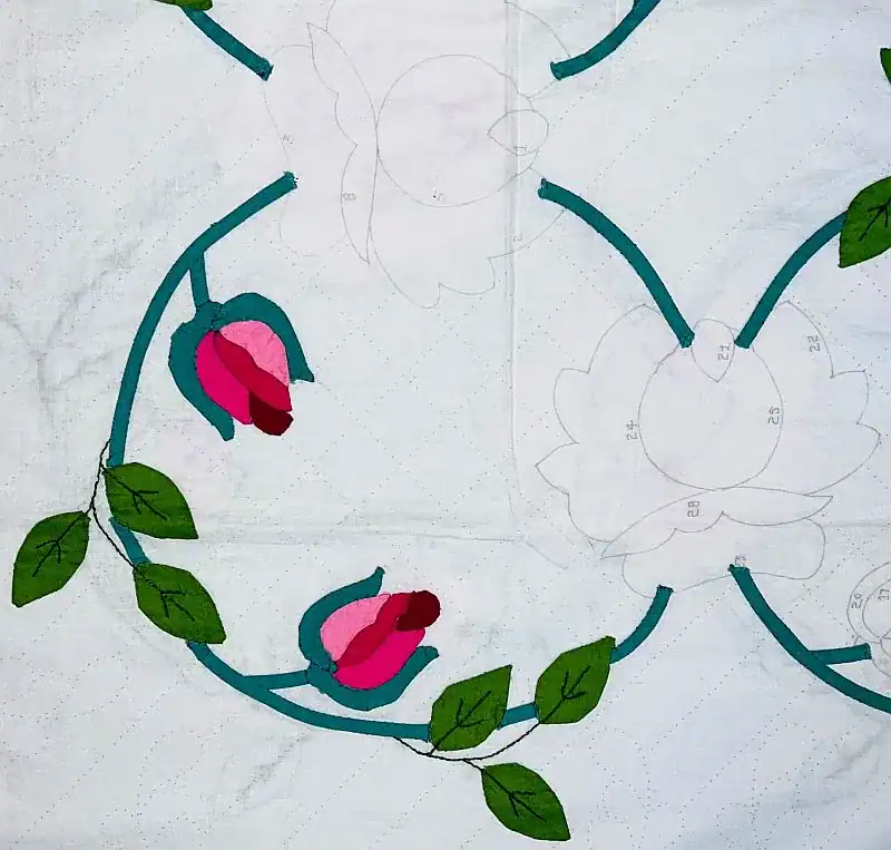 A partially completed quilt features teal stems, green leaves, and pink flower buds on white fabric, with some areas outlined for stitching and patterns visible in pencil—an inviting glimpse into the artistry and tradition explored in Quilt History About and Contact resources.