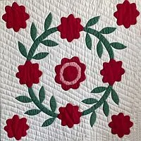 A quilt square with a circular wreath of green leaves and red flowers, including one central red flower, all on a white background with quilted stitching—an exquisite design reminiscent of pieces found in the Quilt History List Archive 1996.