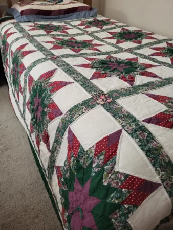 A neatly made bed with a colorful patchwork quilt featuring red, green, and purple star patterns, bordered by floral sashing, and matching pillow shams at the head of the bed.