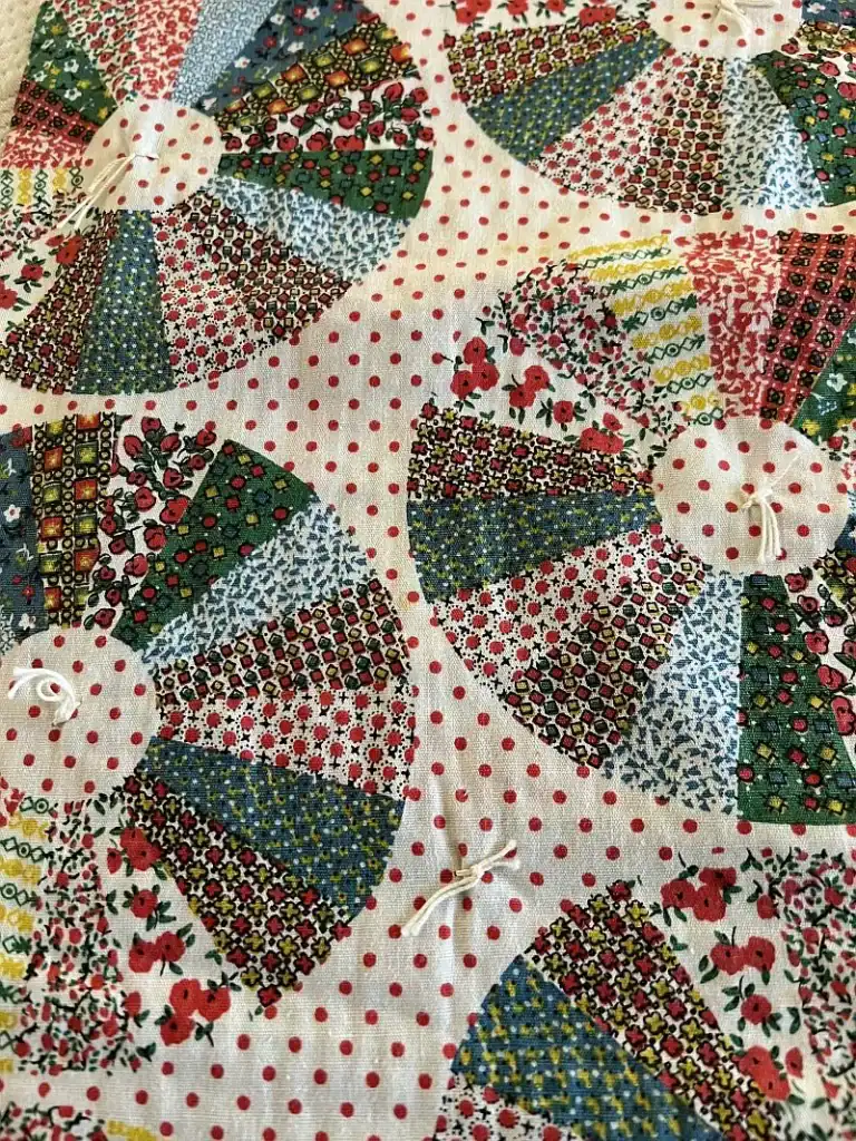 Cheater-Cloth Dresden Plates Quilt fabric featuring colorful, patterned fan shapes stitched onto a white background with red polka dots. The fans use various floral and geometric prints, and each has a small knotted detail at the center.