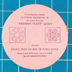 A pink paper template labeled Grandmother Clarks Cutting Diagram B for Dresden Plate and Yo-Yo, Puff, or Bed of Roses quilts, with two square diagrams, on a blue grid background.