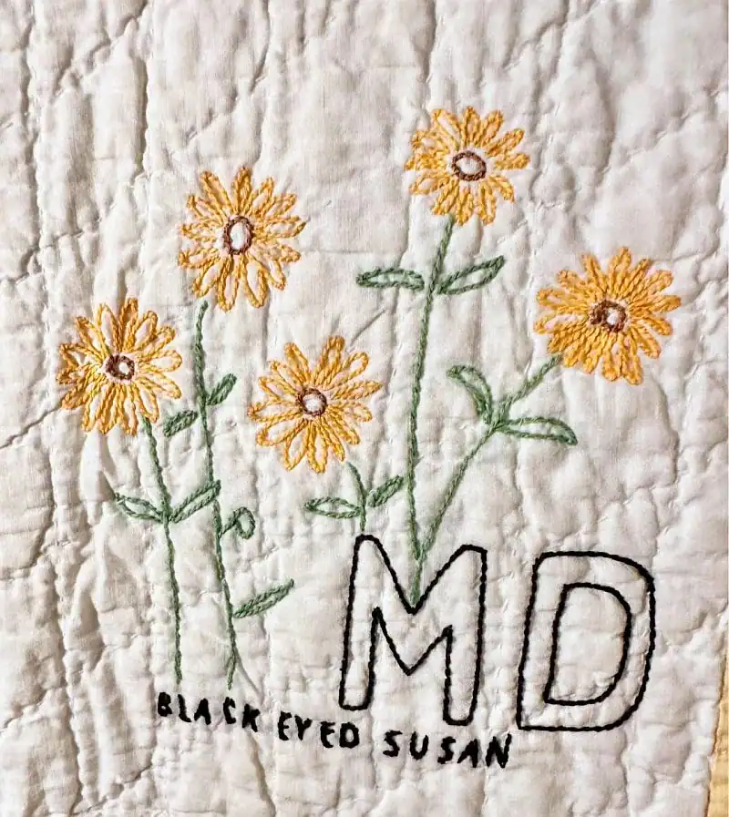 lack Eyed Susan with large letters MD on quilted white fabric, representing Marylands state flower.