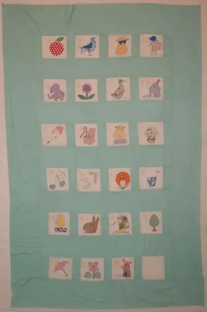 Nancy-Page-Alphabet-Blocks A quilt with a light blue background features 26 square patches, each with a different letter of the alphabet and an illustration matching the letter, arranged in five rows.