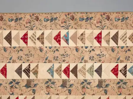 Quilt,_Flying_Geese_pattern_1840-Met A quilt with a floral patterned background and rows of flying geese quilt blocks in various colors including red, blue, brown, and cream.