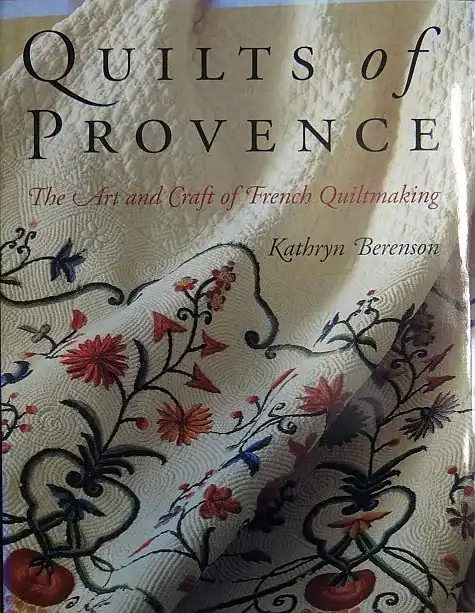 Book cover for Quilts of Provence by Kathryn Berenson, featuring a close-up of an intricately embroidered quilt with floral patterns in red, yellow, and green on a textured white fabric background.