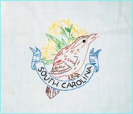 Embroidered image of a brown bird with yellow flowers behind it and a blue banner below that reads South Carolina on a white fabric background, inspired by State Birds and Flowers Outline Embroidery.