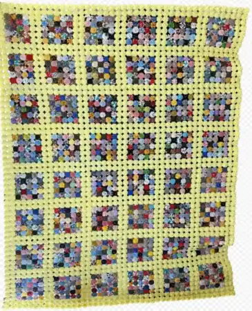 A handmade patchwork quilt with a yellow border and grid. Reminiscent of a Yo-Yo Quilt, each square block contains colorful, patterned hexagons arranged in a flower-like design. The quilt has a slightly uneven edge.