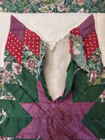 A torn patchwork quilt with green, purple, and red fabric pieces, some floral and polka-dotted, revealing white batting beneath the damage.