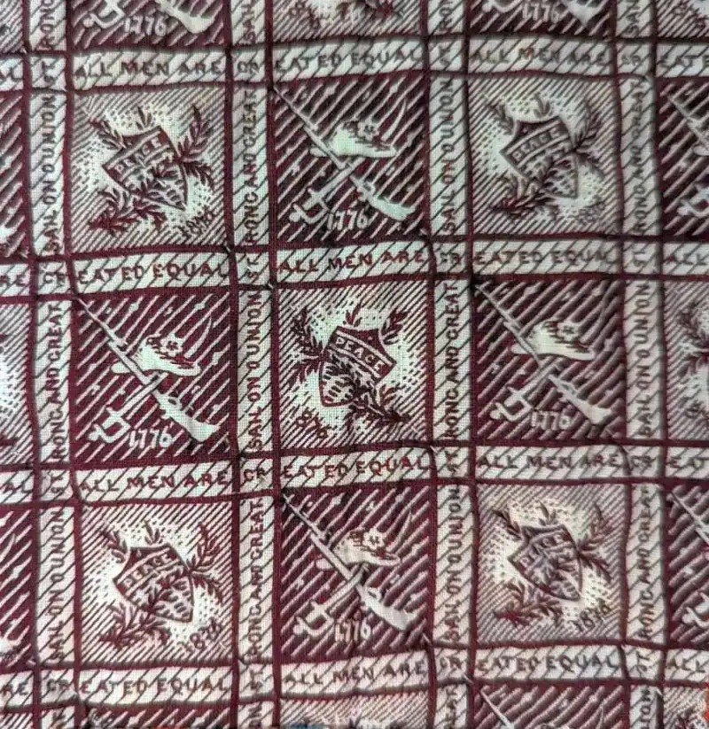 A patterned fabric with repeated squares showing crossed rifles, a hat, 1776, and the word PEACE. The border text reads EQUAL RIGHTS FOR ALL MEN. The design is in shades of brown and cream.