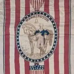 Vintage quilt with red and white stripes, a central oval frame showing George Washington beside a horse, blue star border, and two shield motifs with stars and stripes at top and bottom.