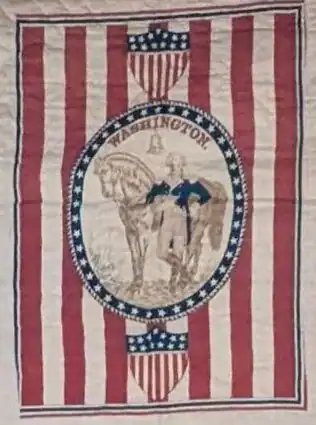 Vintage quilt with red and white stripes, a central oval frame showing George Washington beside a horse, blue star border, and two shield motifs with stars and stripes at top and bottom.