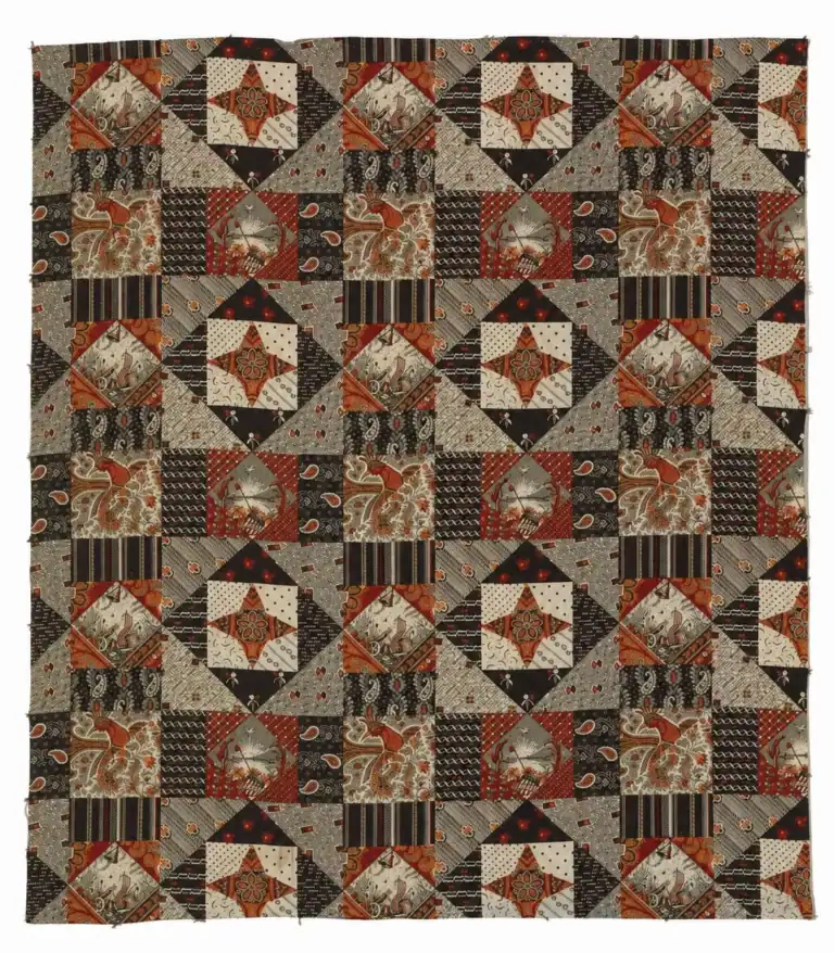 Patchwork quilt with geometric and star patterns in shades of brown, black, cream, and rust orange. Each square features a unique mix of prints—including stripes, dots, paisley, florals, and striking touches inspired by 1876 Centennial Fabric. The layout forms a repeating grid.