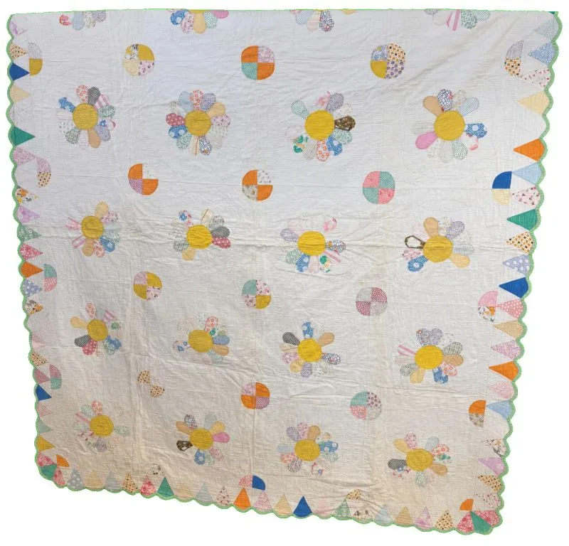 A handmade quilt with a white background, decorated with colorful patchwork flowers and circle patterns, and a scalloped edge bordered with alternating colored triangles.
