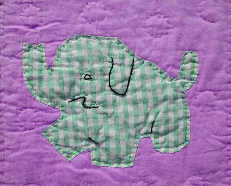 Patchwork quilt with a green and white checkered elephant stitched onto a purple fabric background, with simple black thread details for the elephants face and ear.