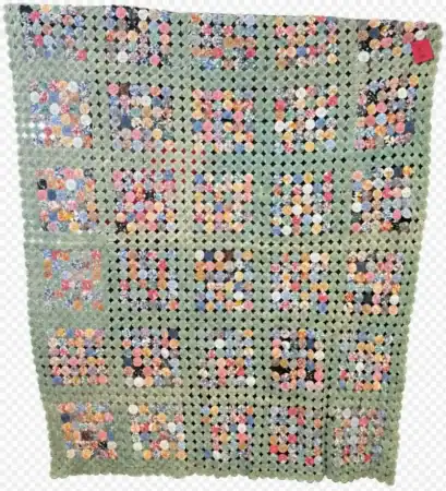 A patchwork quilt with a green border and 25 square sections, each made of colorful hexagon pieces in various patterns; the quilt has a tag on the upper right corner.