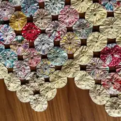 more-finishing-details for a yo-yo-quilt Colorful yo-yo quilt made from small, circular fabric pieces sewn together, displayed on a wooden surface. The quilt forms a triangular shape in the image.