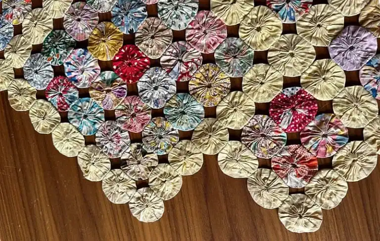 more-finishing-details for a yo-yo-quilt Colorful yo-yo quilt made from small, circular fabric pieces sewn together, displayed on a wooden surface. The quilt forms a triangular shape in the image.