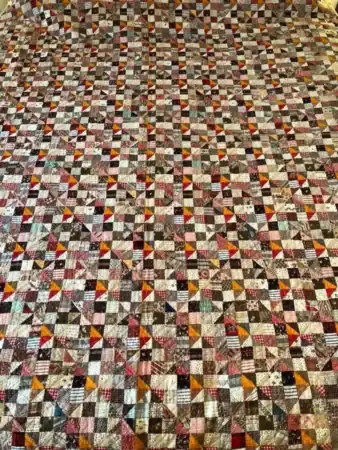 A large cheater cloth faux patchwork quilt featuring hundreds of small, multicolored triangles and squares arranged in a repeating geometric pattern, creating a vibrant, cozy design.