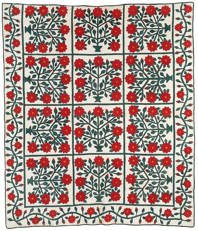 A quilt with a grid of red floral patterns and green stems on a white background, bordered by a matching floral and vine design.