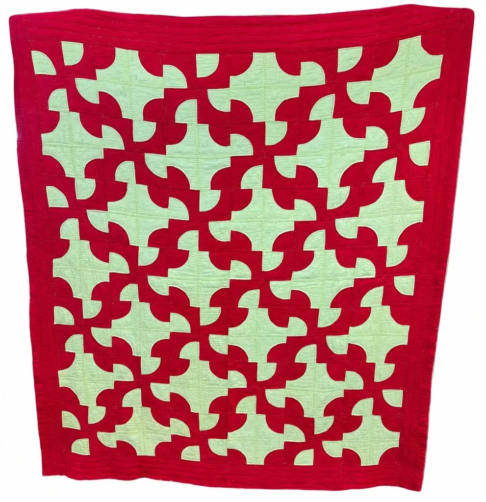 red-and-yellow-drunkards-path quilt A quilt featuring a red geometric pattern on a pale green background, with interlocking curved shapes and a solid red border around the edges. The design creates a bold, repeating abstract motif.