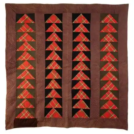 A quilt with a brown border features vertical stripes of geometric red, black, and brown triangle patterns, resembling flying geese shapes, arranged in rows on a square background.