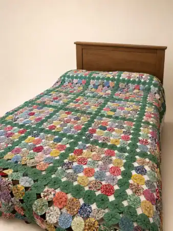 Yo-Yo on bedA wooden bed with a colorful, patterned quilt made of multicolored fabric circles and green connecting pieces, displayed against a plain background.