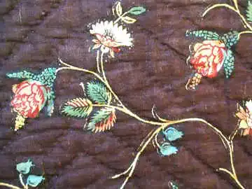 Quilted fabric with a dark brown background, featuring a floral pattern of red, white, and green flowers and leaves on thin, curving stems.