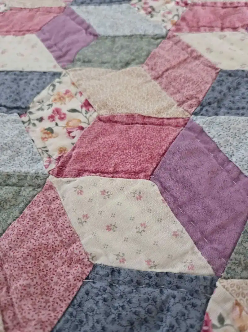 A close-up of a patchwork quilt featuring various pastel fabrics with floral and geometric patterns, sewn together in a diamond and triangle design.
