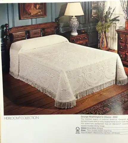 Geo-Washington-Quilt A vintage wooden bed with a white, textured, fringed bedspread in a traditional room. A lamp, framed art, and decor are visible, giving the space a classic, elegant look.