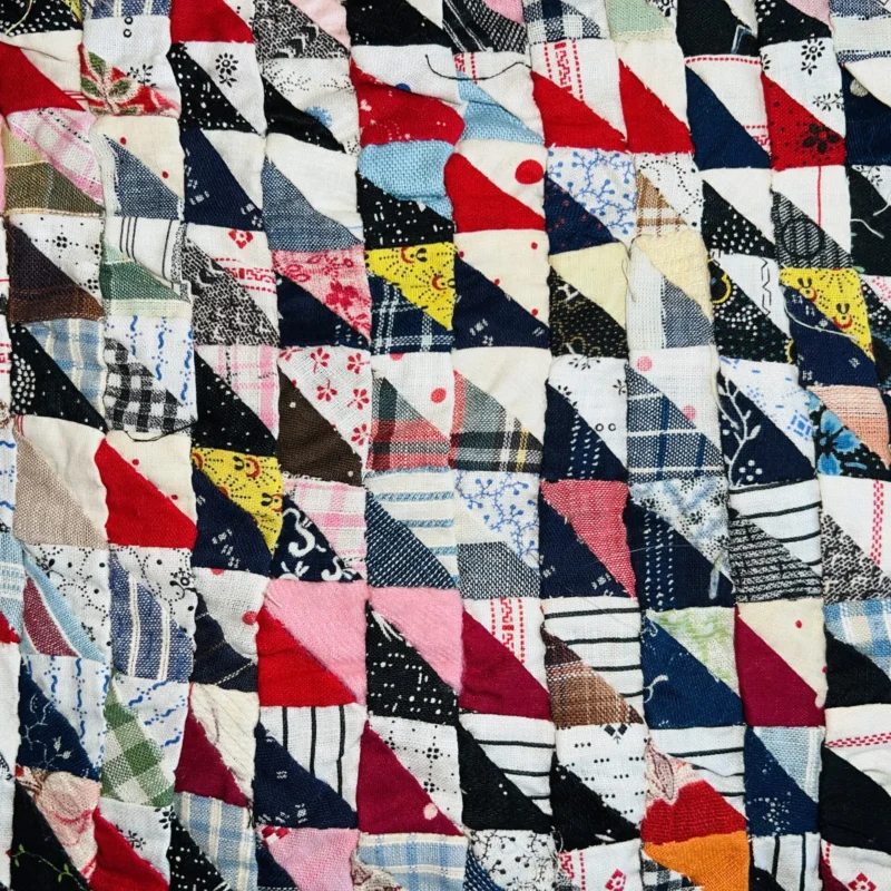 A colorful patchwork quilt made of small triangular fabric pieces in various patterns, including stripes, plaids, florals, and solids, sewn together in a repeating geometric design.