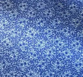 Lancaster-Blue-Double-Blue Blue fabric with a textured pattern of swirling, interconnected lines and dots, creating a decorative and abstract design. The surface appears soft and woven.